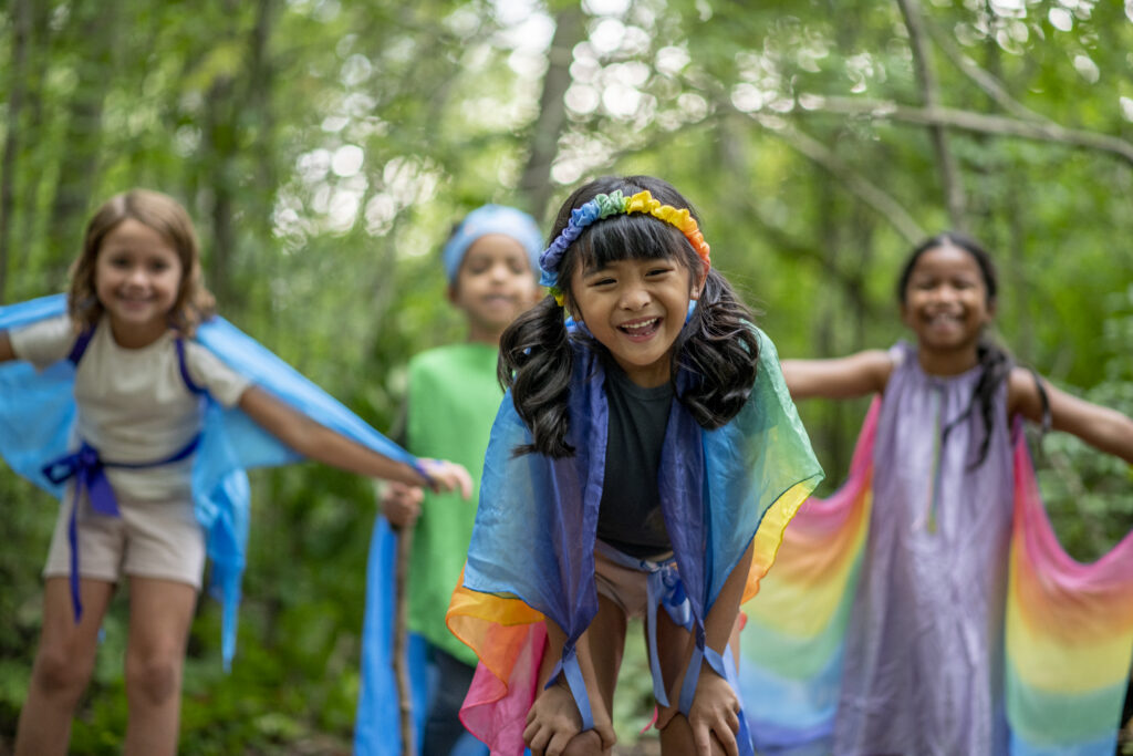 Children play together, using their imagination. They are in deciduous forest and it is summertime.