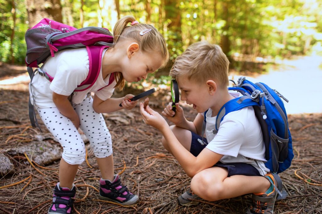 Children siblings exploring nature with magnifying glass. Curious kids in forest discovering learning about nature.