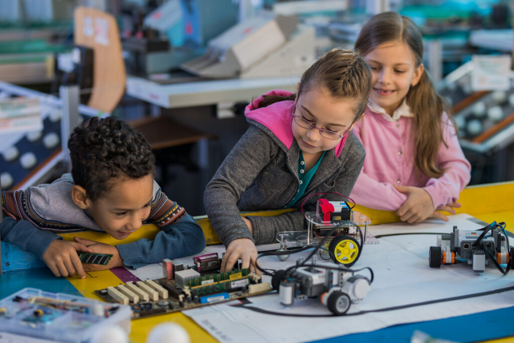 Group of small kids working on motherboard and robots in laboratory.